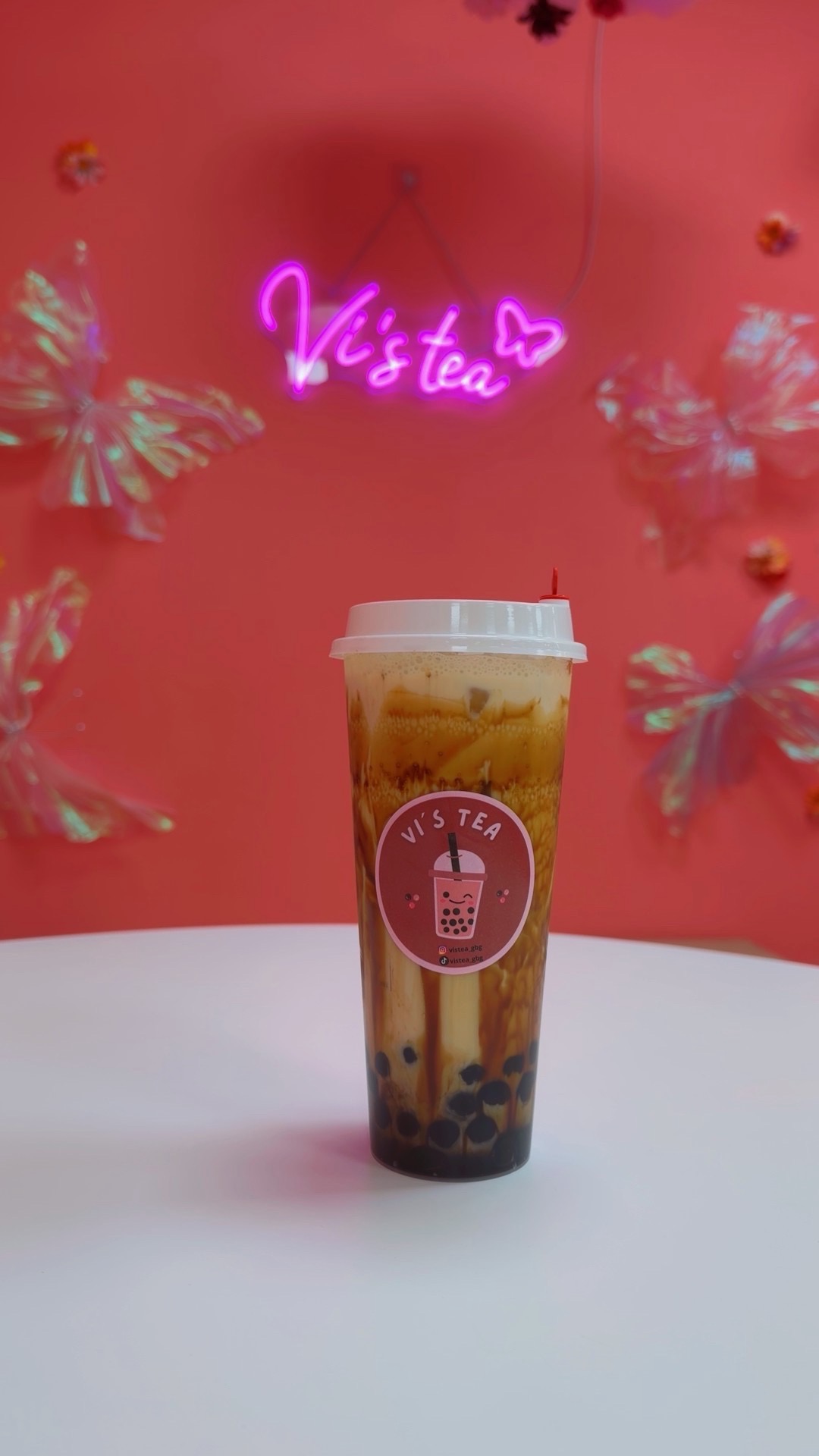 Brun sockermjuk bubble tea med tapiokapärlor framför Vi's Tea neonskylt